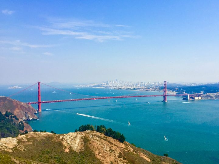 The Golden Gate Bridge spans green waters of San Francisco Bay and the Golden Gate channel. The City of San Francisco is seen in the distance. 