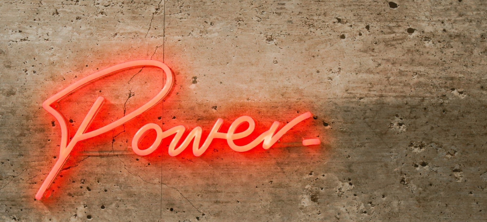 a neon sign that reads power on a concrete wall
