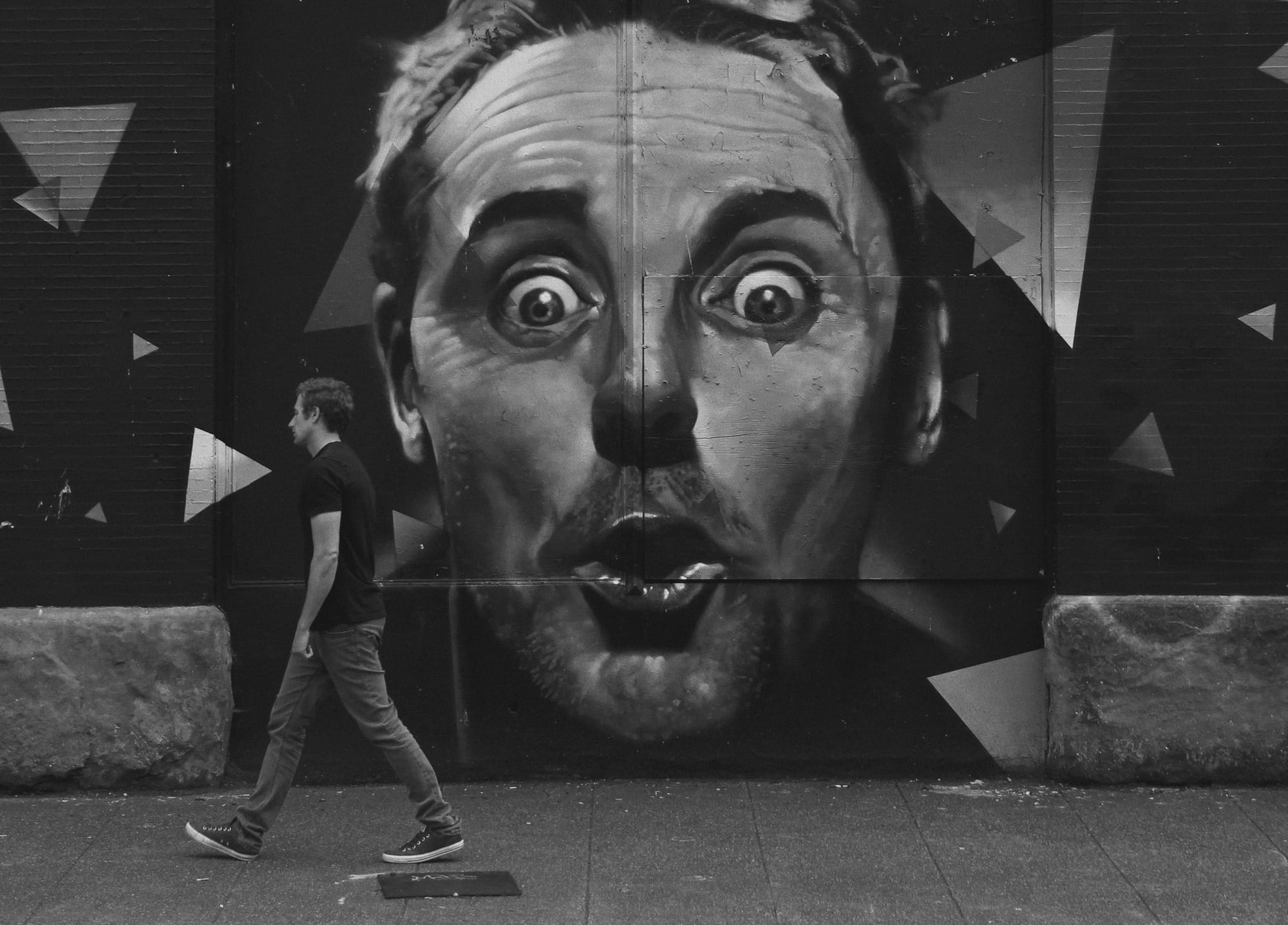 grayscale photo of man walking beside painted wall