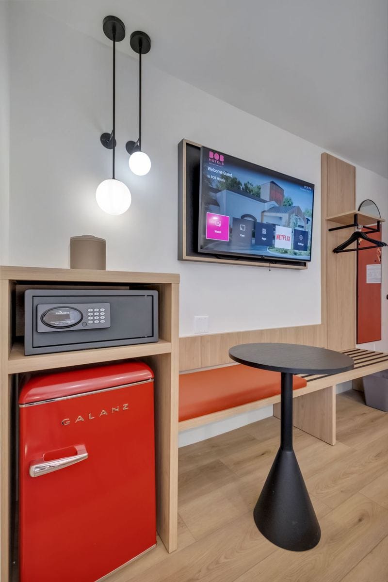A red retro mini fridge, in-room safe and smart TV in a BOB Hotels room