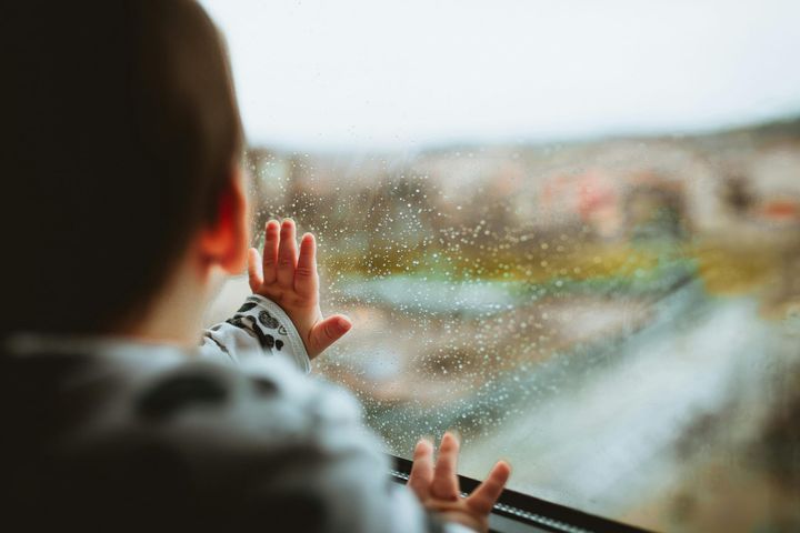 toddler pressing a hand to a rainy window and looking into a blurred world