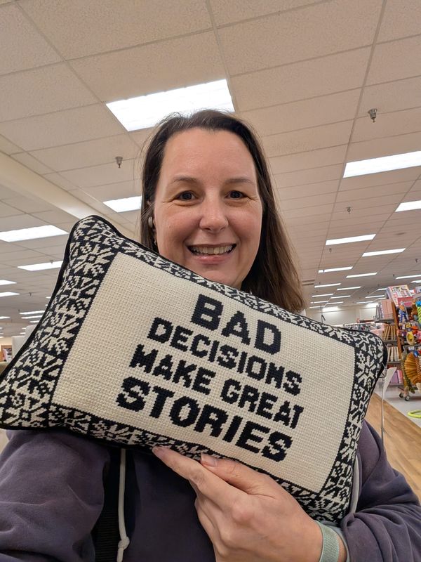Angela "Surya" holding a pillow that says, "Bad Decisions Make Great Stories."