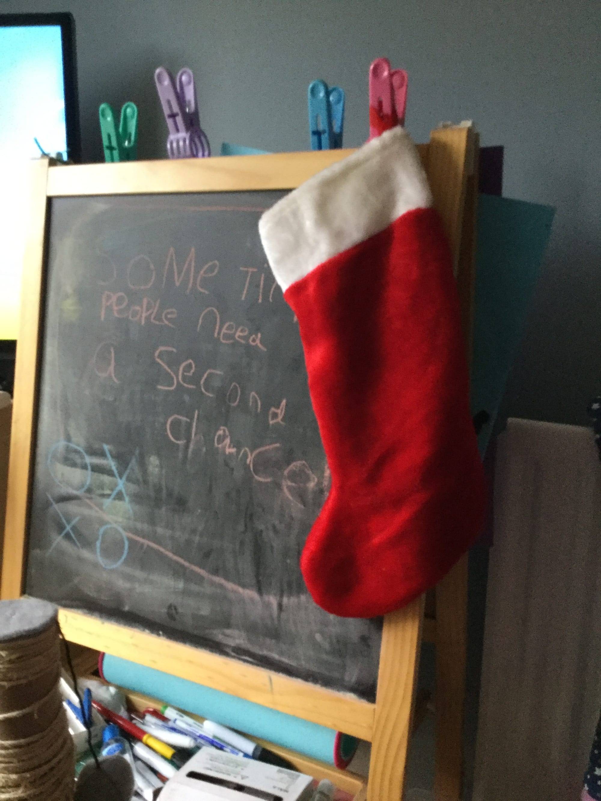 A child's blackboard, with a child's (my daughter's!) writing saying "sometimes people need a second chance!" There's a red and white Chistmas stocking handing on the corner of the blackboard.