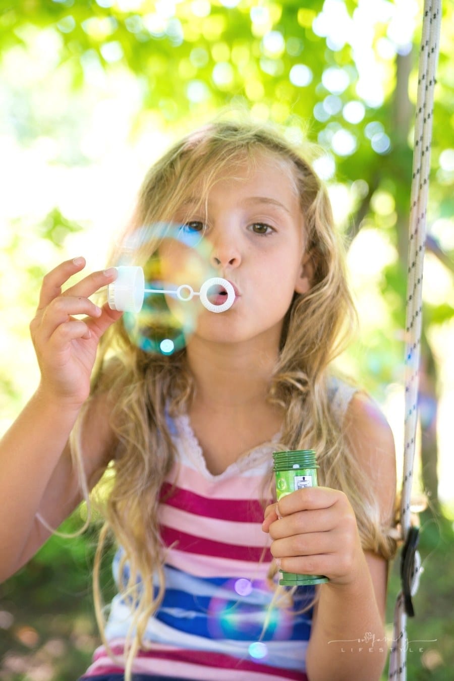 girl blowing bubbles while sitting on a swing