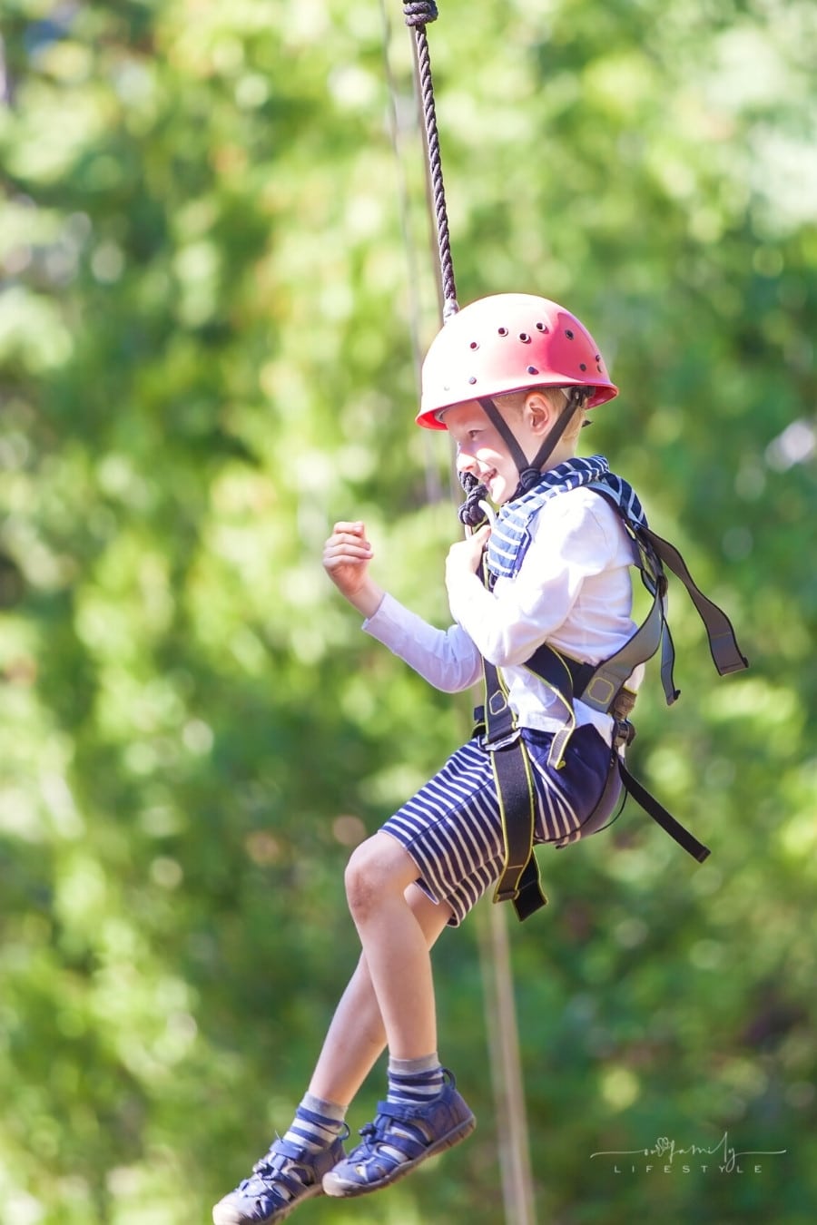 little boy is ziplining with helmet on at outdoor treetop park