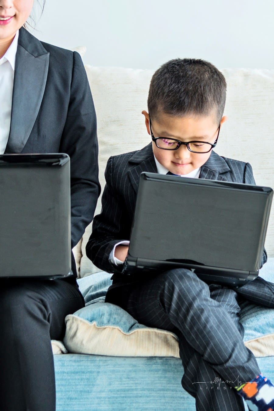 Businesswoman and her son holding their laptop and sitting on sofa at home.