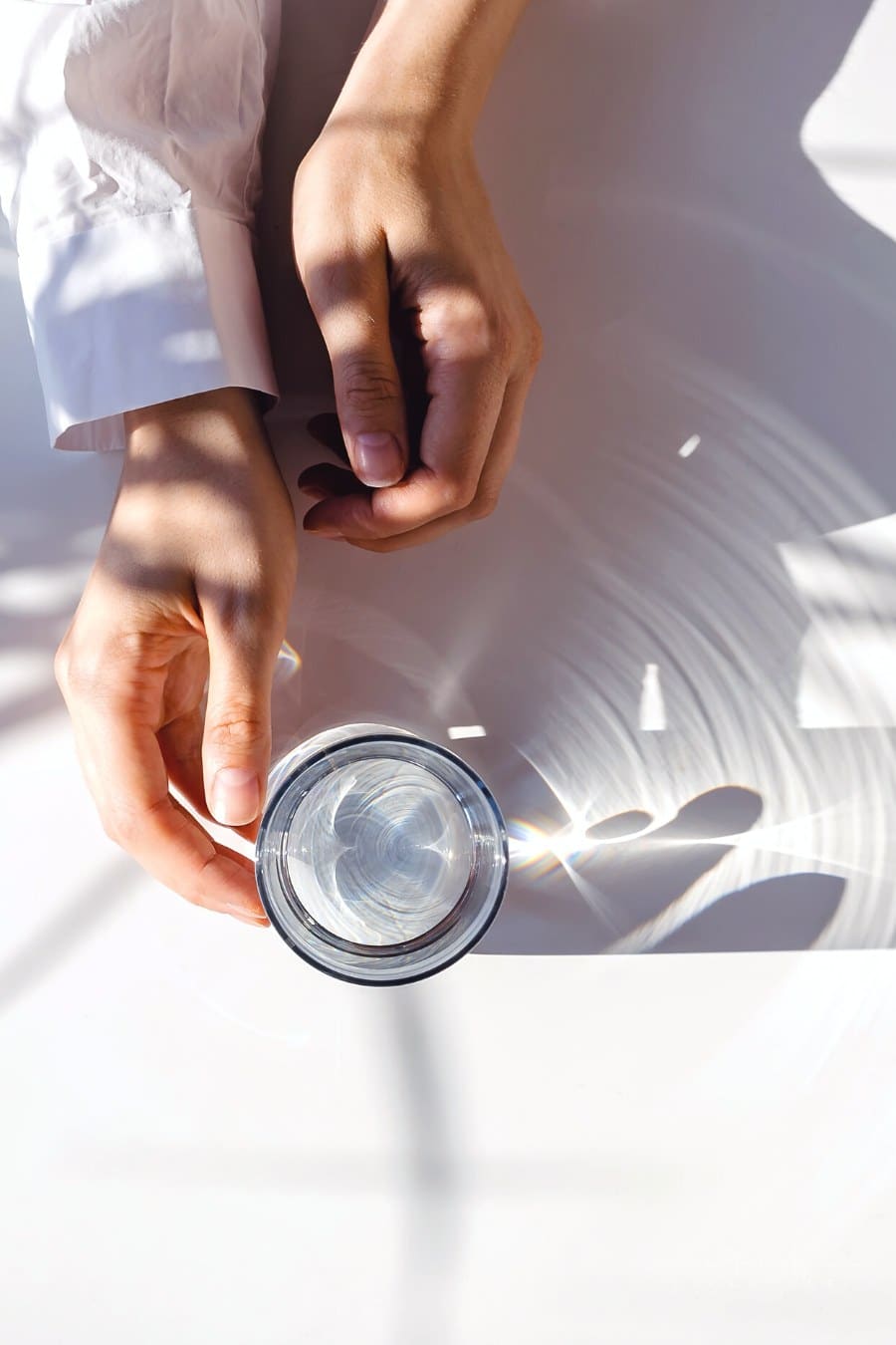 woman's hands wrapped around a glass of water on a white table
