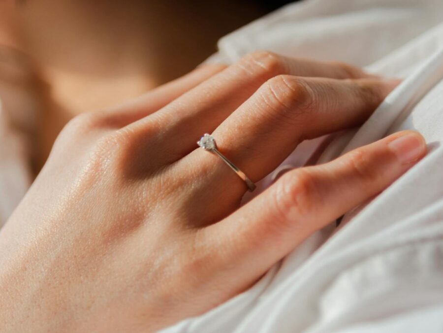 A close-up view of an elegant engagement ring on a woman's hand in soft lighting.