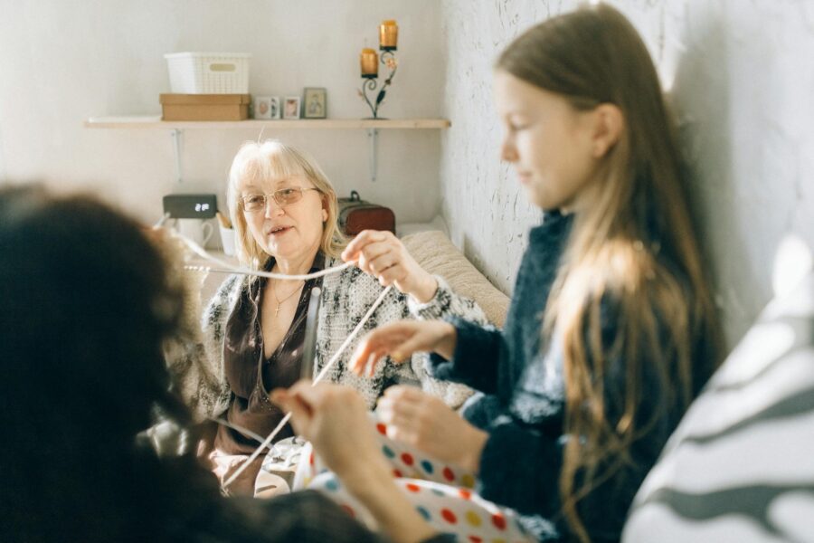 A cozy family moment with grandmother teaching granddaughter crochet indoors.