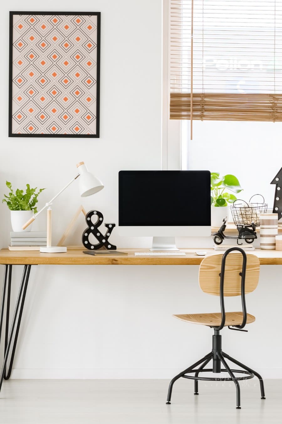 Large industrial desk with a computer by a window, a wooden bookcase and posters on a white wall in a stylish, scandi home office interior