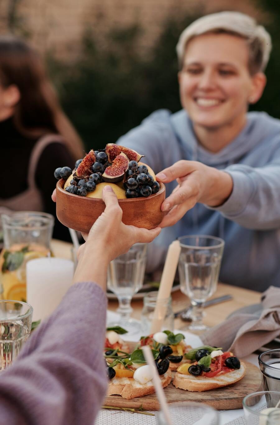 A group of friends enjoying an outdoor dinner, sharing a bowl of fruit in a garden setting.