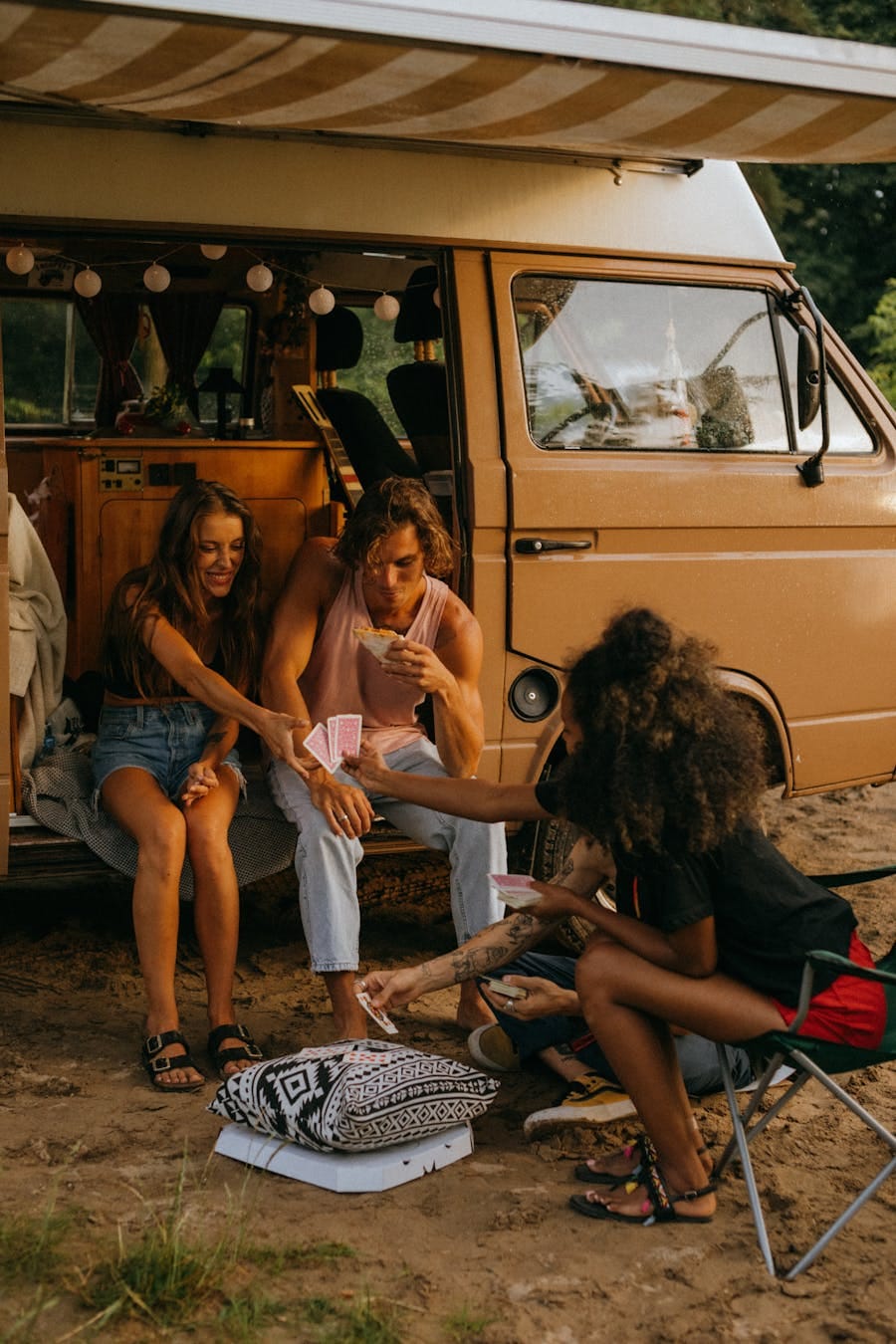 A group of young friends enjoying a card game next to a campervan during their camping holiday.