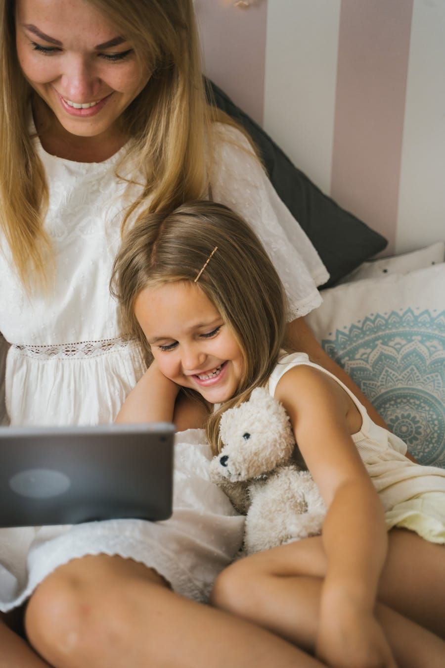 A joyful mother and daughter bonding over a tablet in a cozy indoor setting.