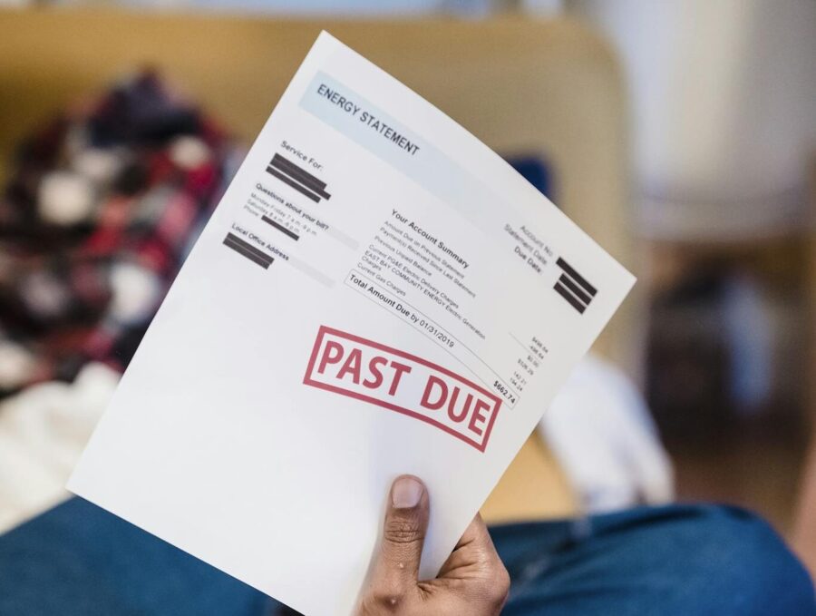 A man holding a past due billing statement while lounging indoors, expressing financial stress.