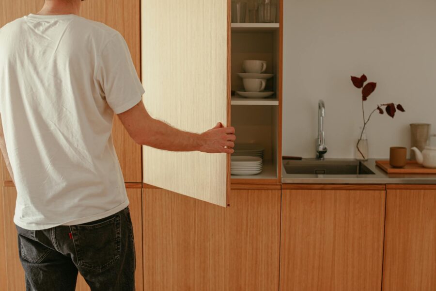 A man opens a wooden kitchen cabinet in a modern minimalist kitchen.