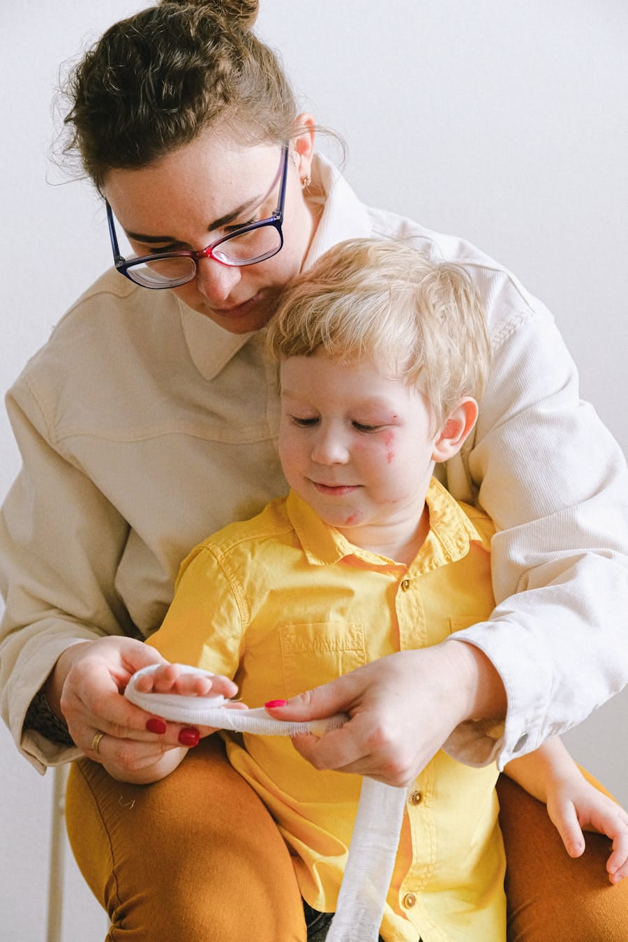 A mother attentively applies first aid to her young son indoors.