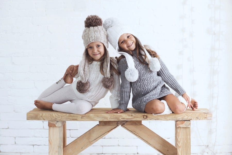 child models wearing knitted trendy winter clothes posing over white brick wall