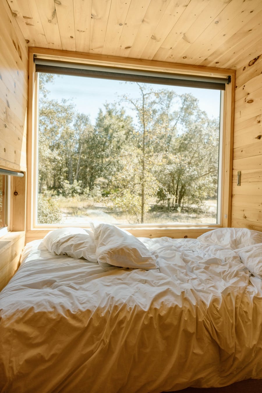 A peaceful cabin bedroom with a large window view of a lush forest enhances relaxation and tranquility.