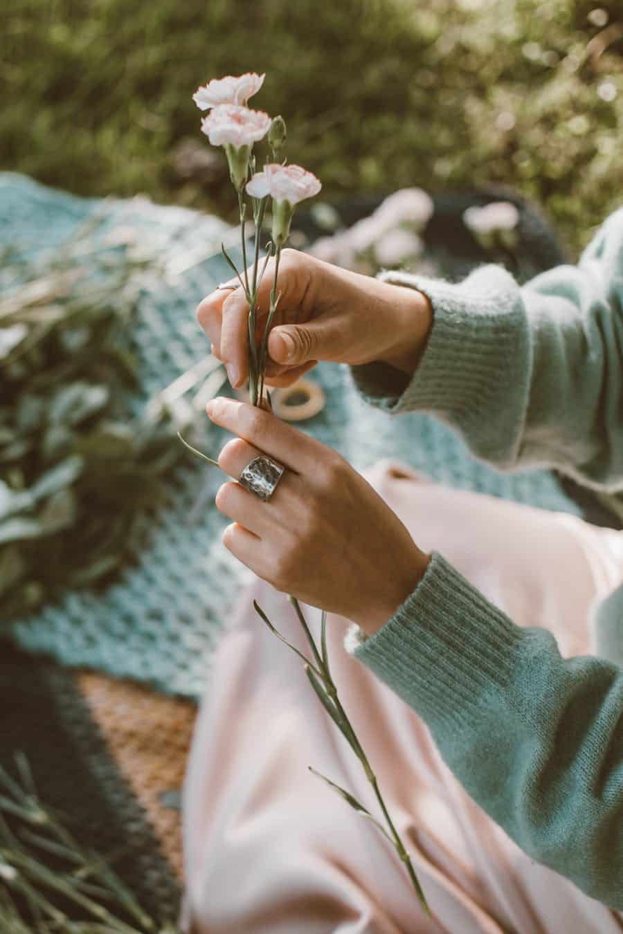 A person in a sweater holds delicate flowers, creating an artistic arrangement.
