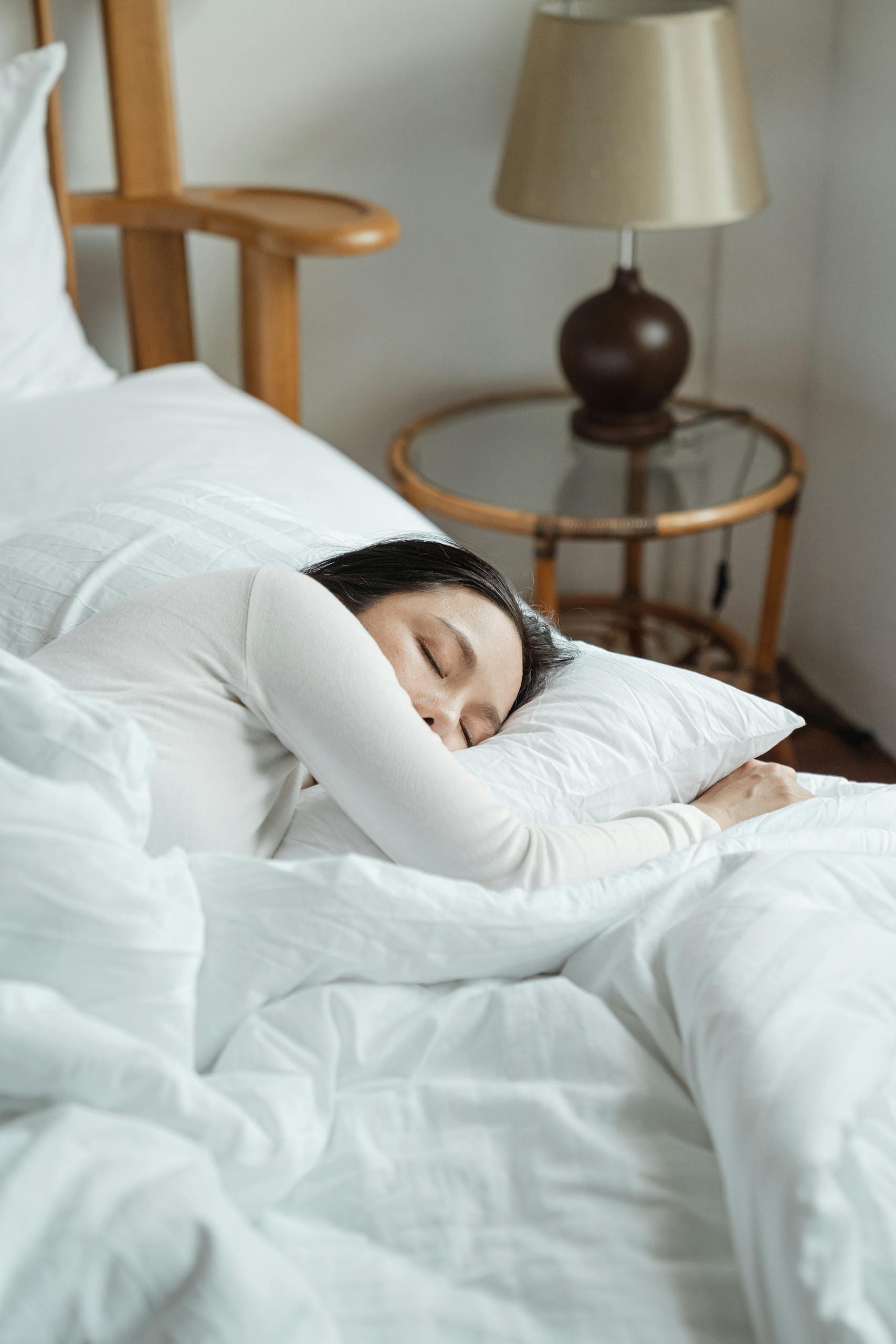 A serene scene of a woman sleeping peacefully on white bedding in a cozy bedroom.