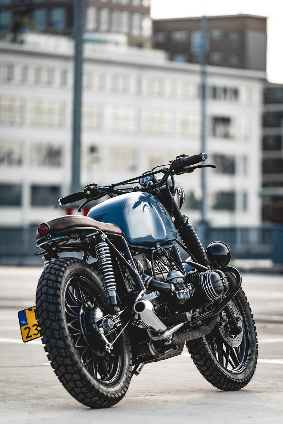 A sleek cafe racer motorcycle parked on asphalt with modern architecture in the background.