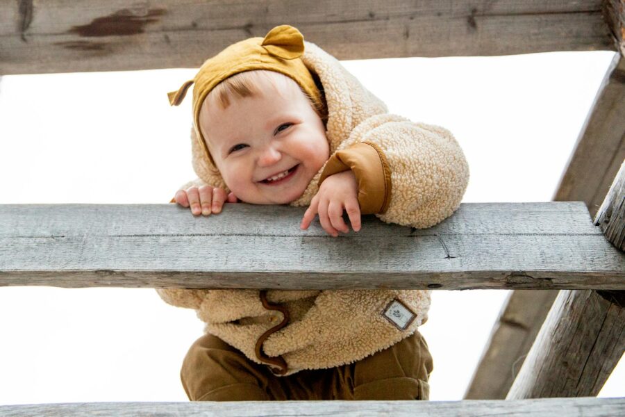 A smiling baby in a cozy teddy bear jacket plays outdoors, showcasing innocence and happiness.