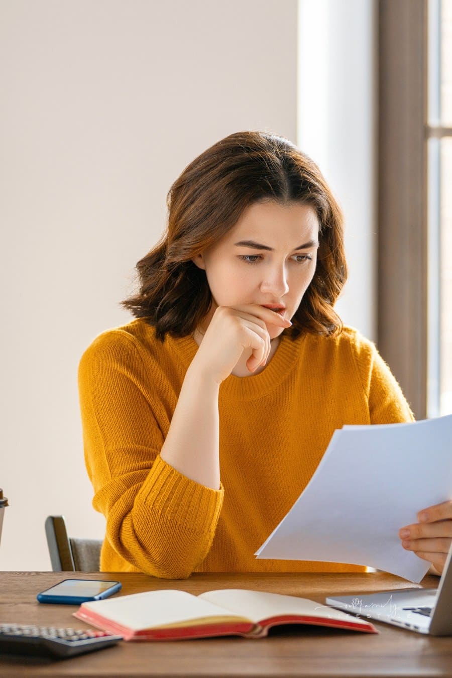 woman staring diligently at paper in front of laptop