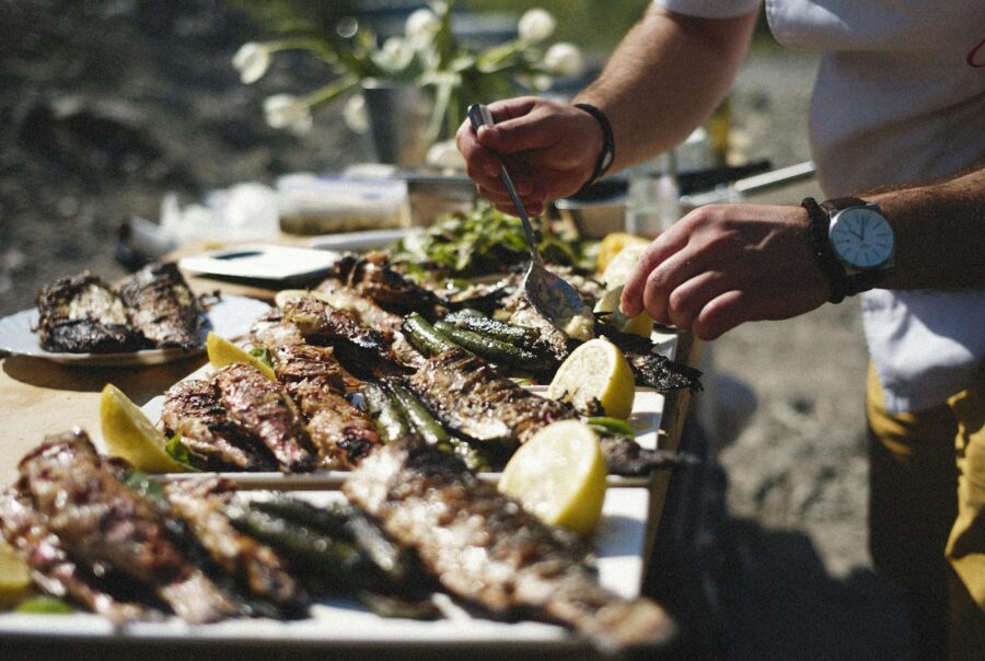 A vibrant outdoor barbecue with grilled fish and fresh lemons being prepared by hand.