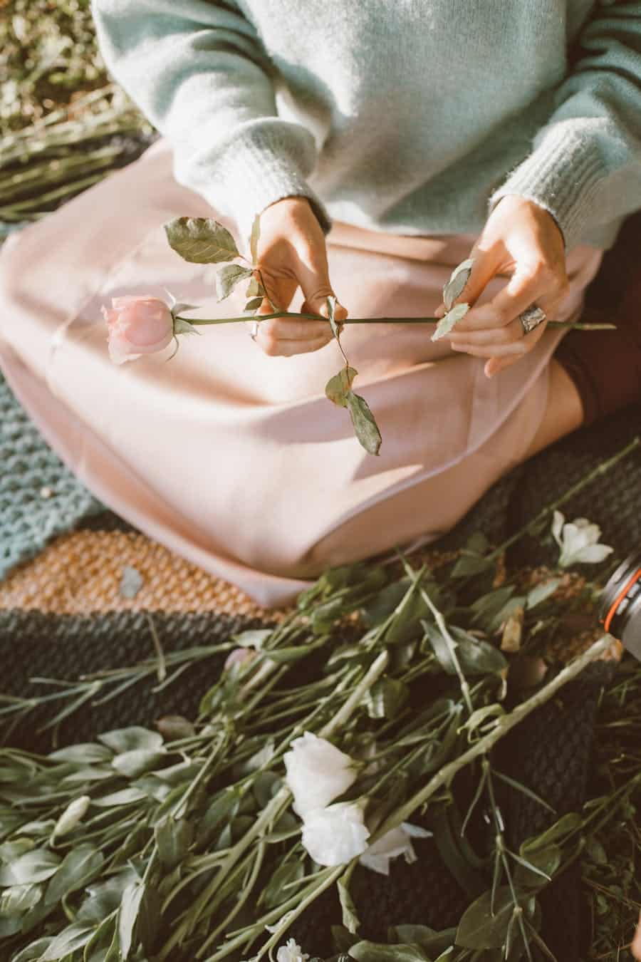 A woman arranging pink and white flowers while sitting outdoors on a sunny day.