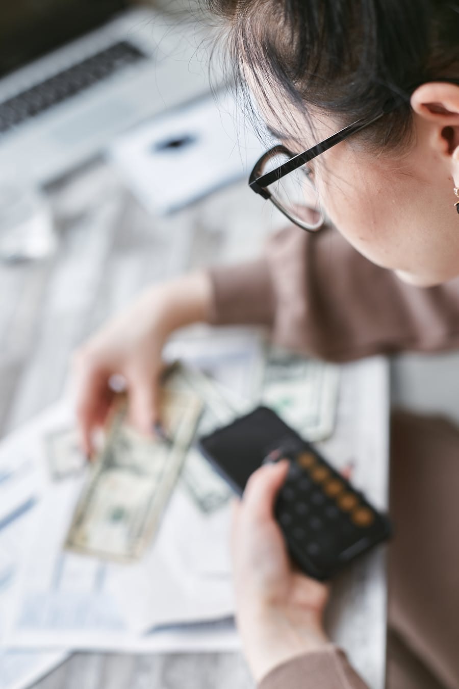 A woman calculates finances using a calculator with banknotes and documents on the table.
