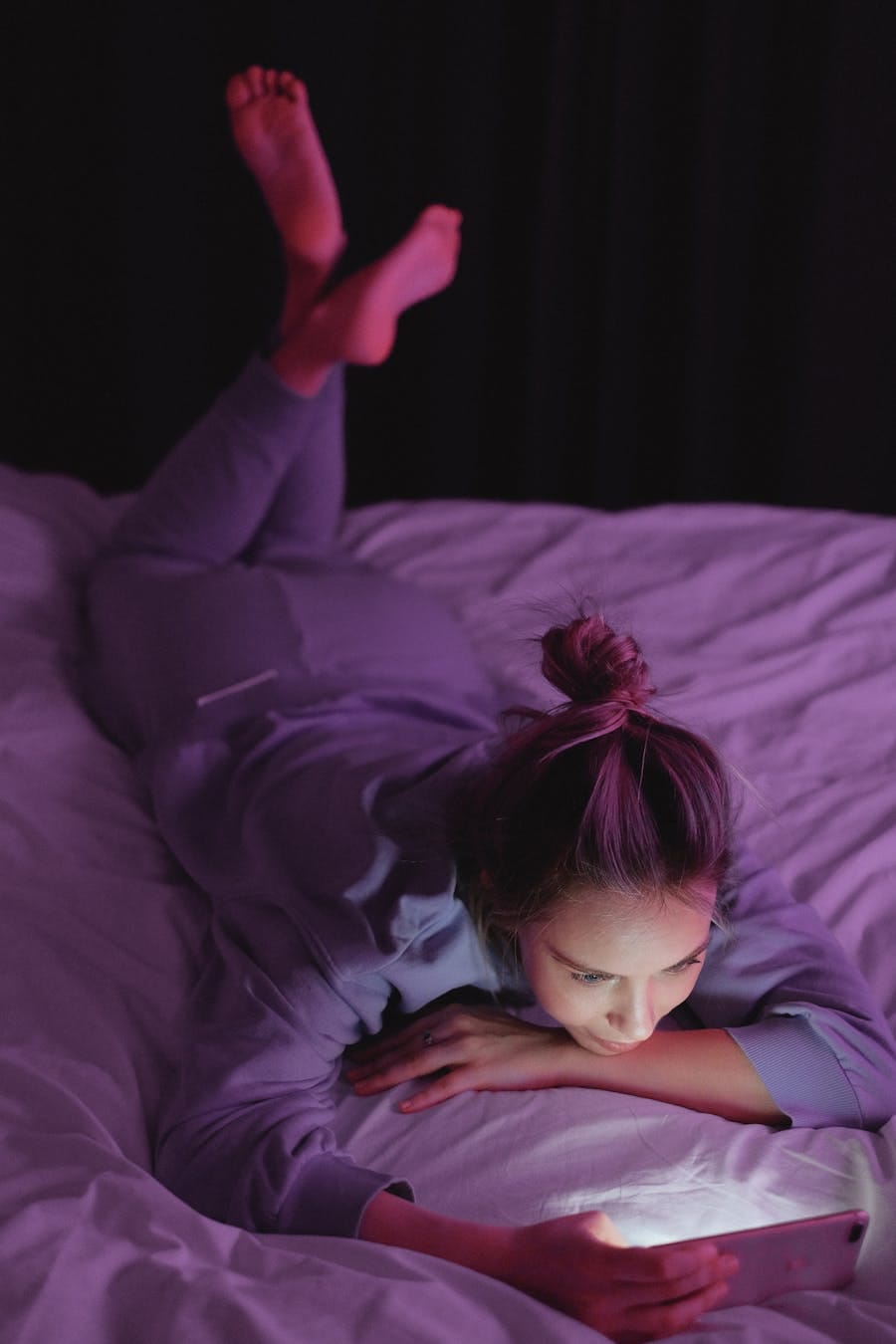 A woman lying on a bed using her smartphone at night, illuminating her face.