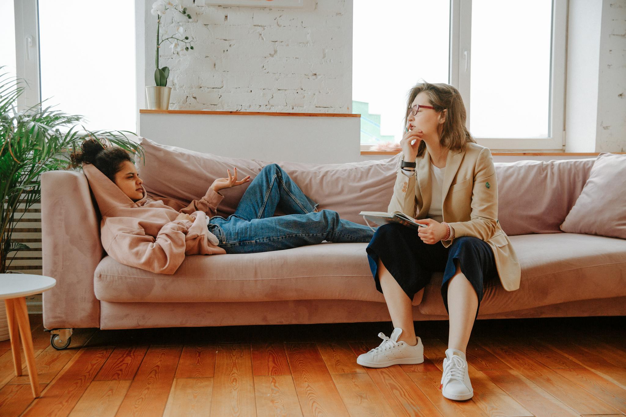 A young woman in a hoodie engages with a therapist during a counseling session indoors.