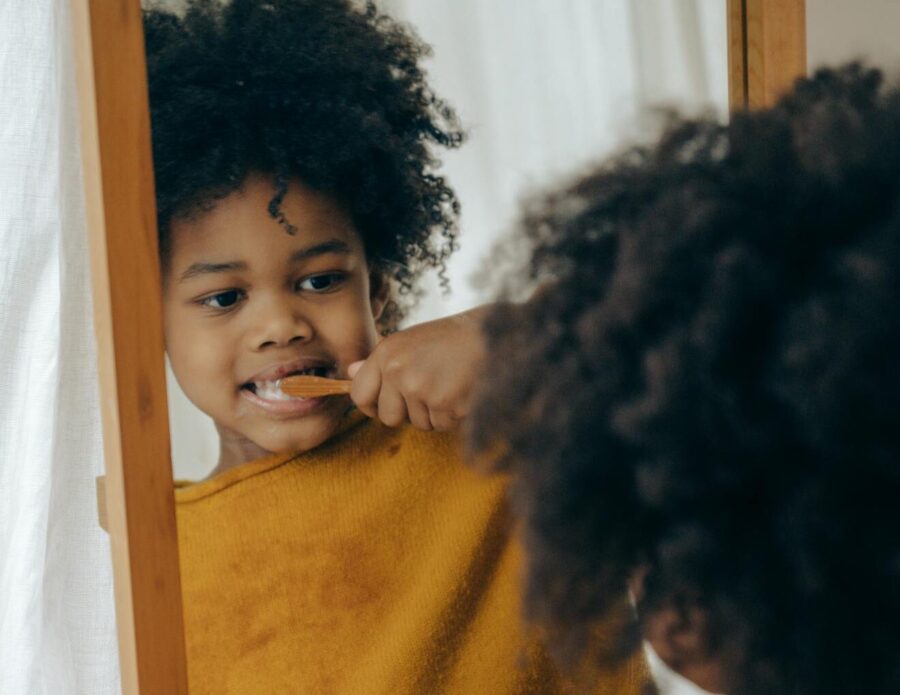 Adorable child brushing teeth with orange toothbrush in front of mirror, promoting dental care routine.