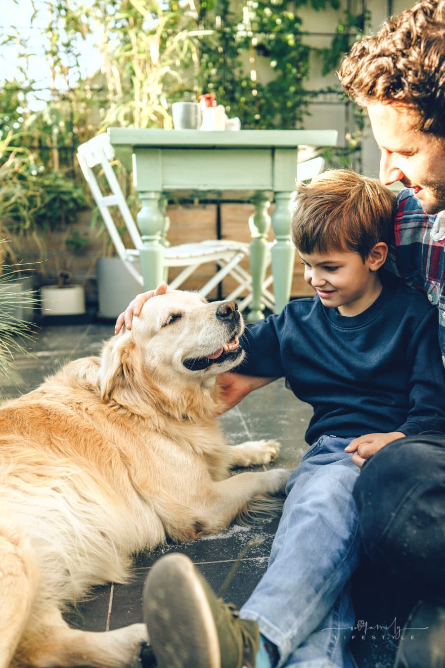 father and son petting their family dog, a Labrador retriever