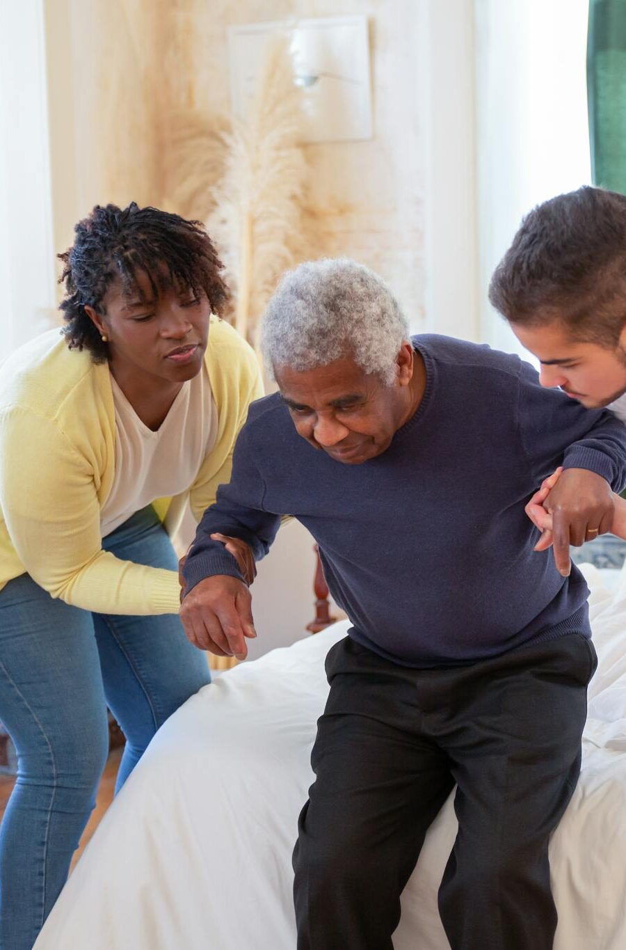 An elderly man receiving assistance from caregivers in a cozy home environment.