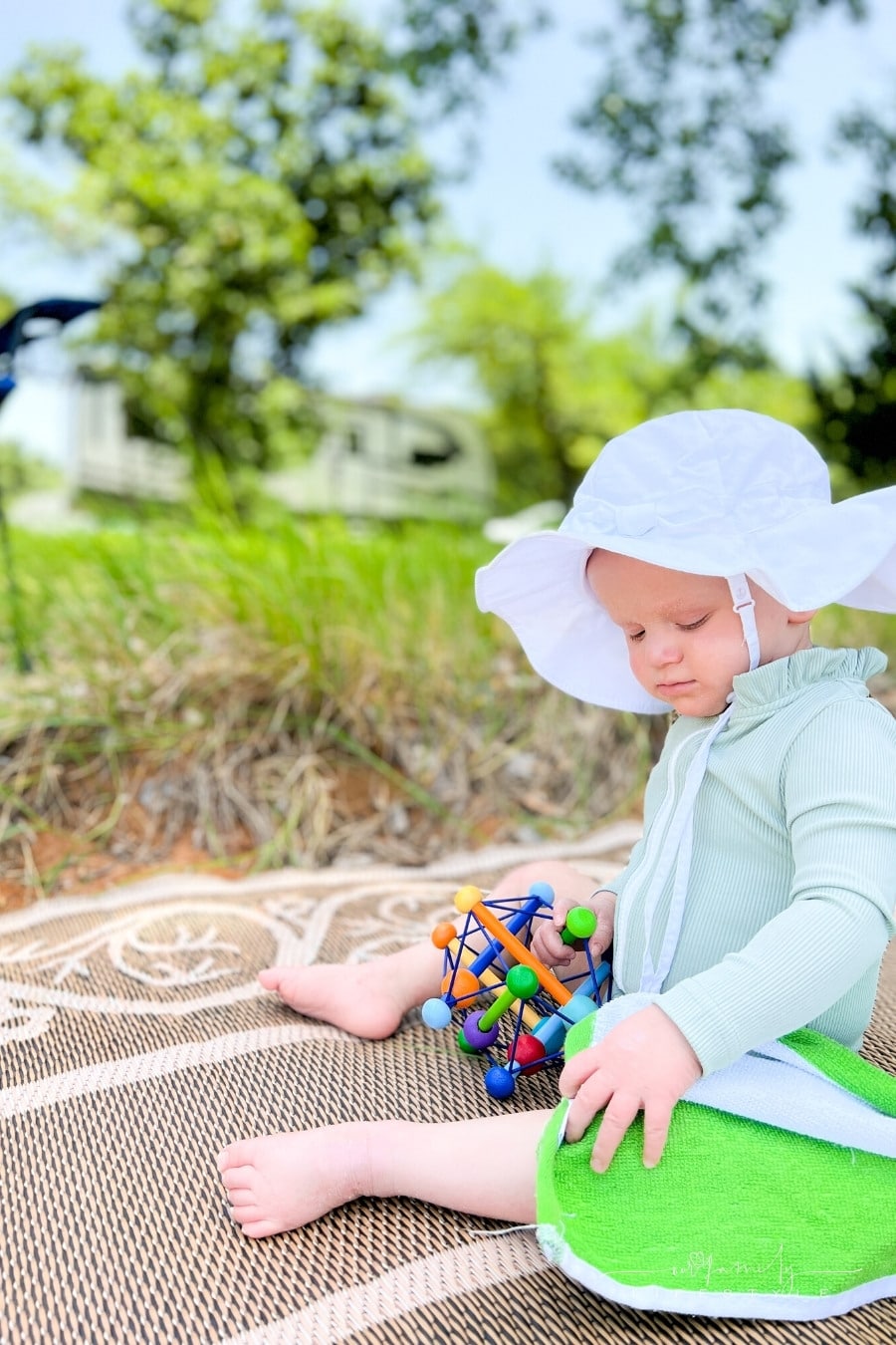 baby wearing sunhat playing with a toy while sitting in front of an rv trailer