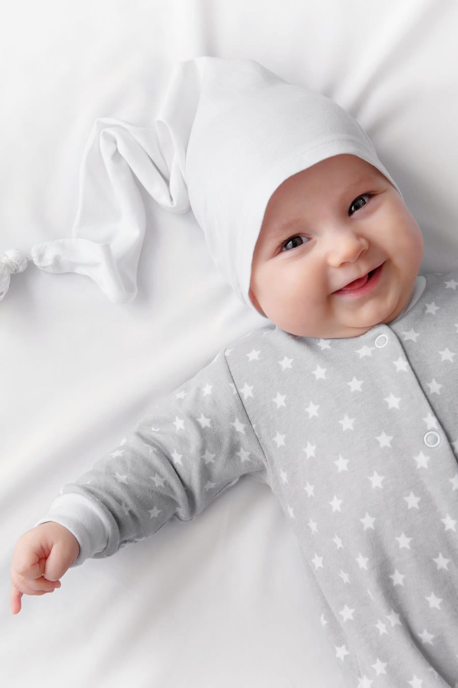 happy baby lying on sheet wearing pajamas and a night cap