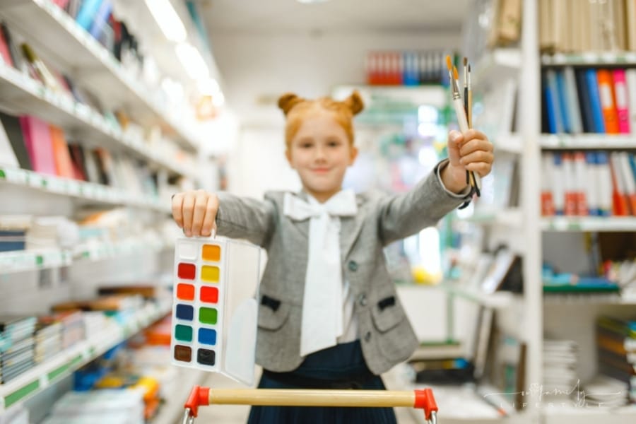 school girl with watercolor paints and brushes in store aisle