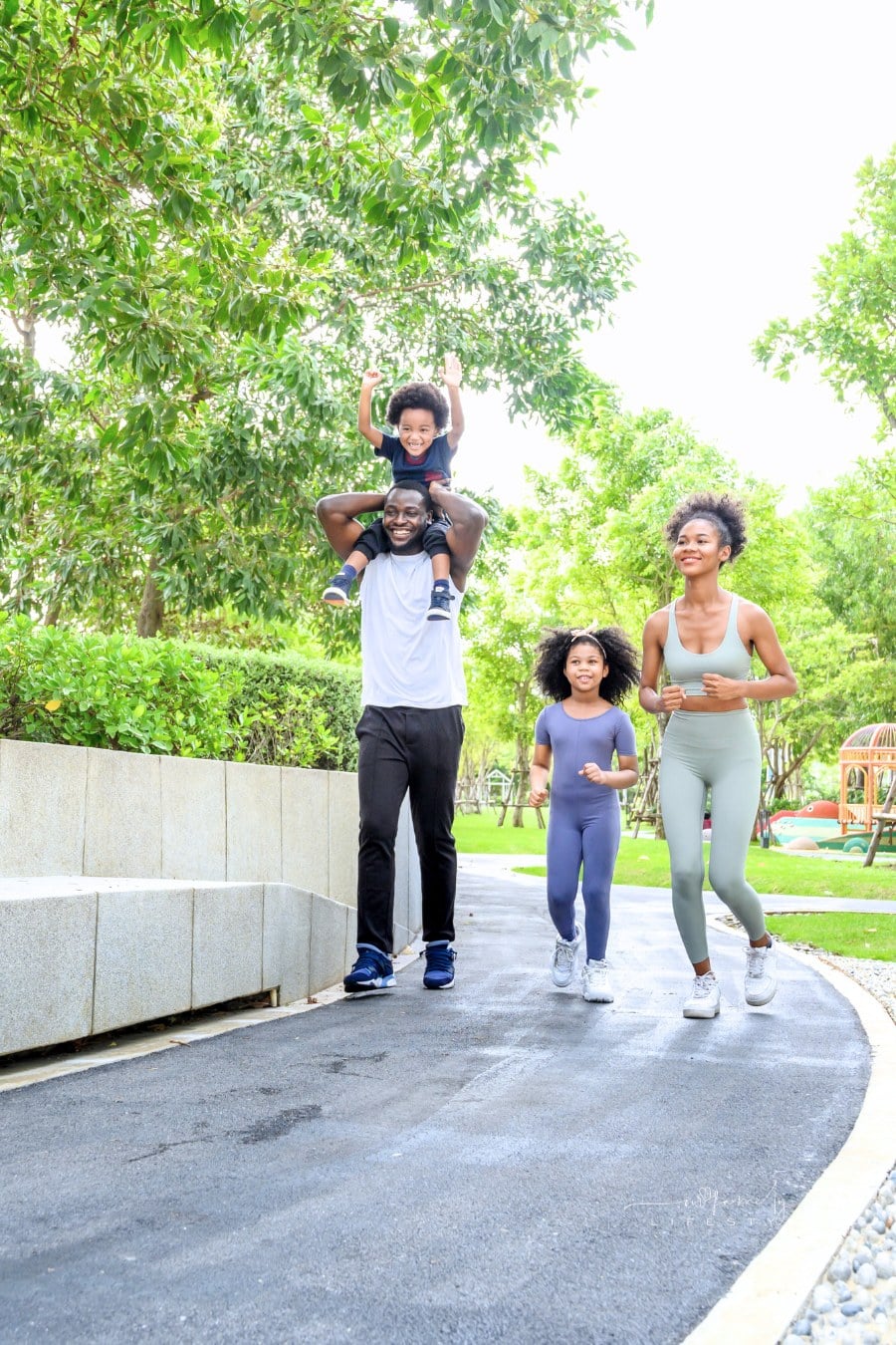 Happy family in sportswear running in public park. father carrying son with mother and daughter. Family exercising together concept.