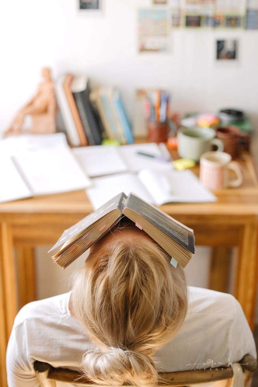 young woman with head thrown back over chair with open book over her face 
