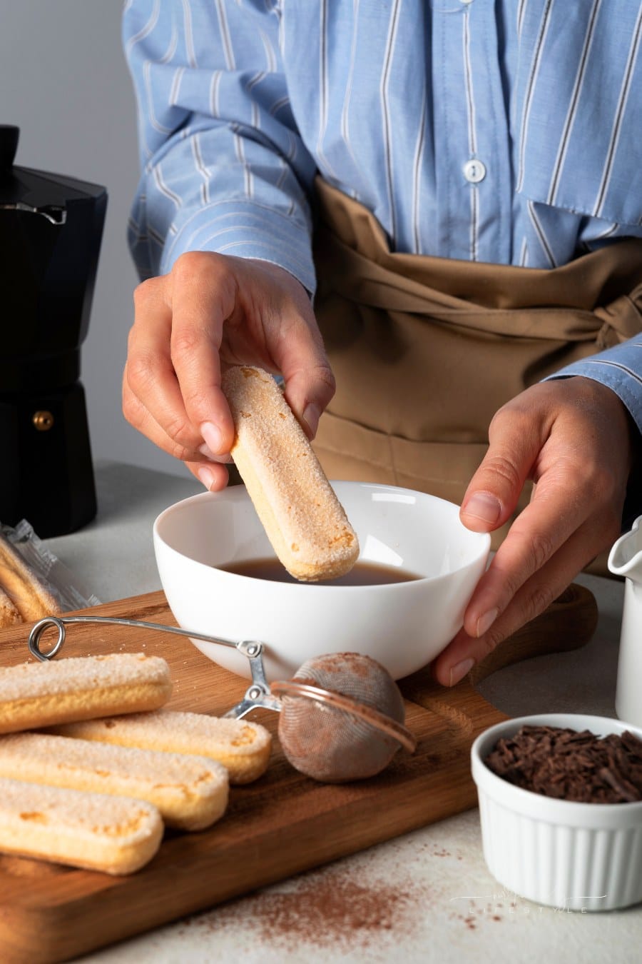 Side view of chef dipping ladyfinger into coffee for tiramisu
