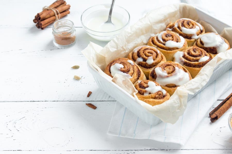Cinnamon rolls or cinnabon, homemade sweet traditional dessert buns with white cream sauce on white wooden background, copy s