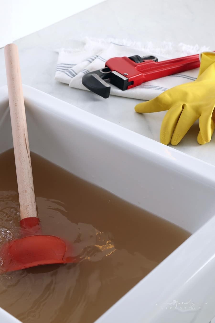 kitchen counter with clogged sink, plunger and plumber's tools