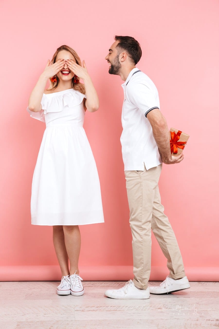man holding gift behind his back for woman covering her eyes