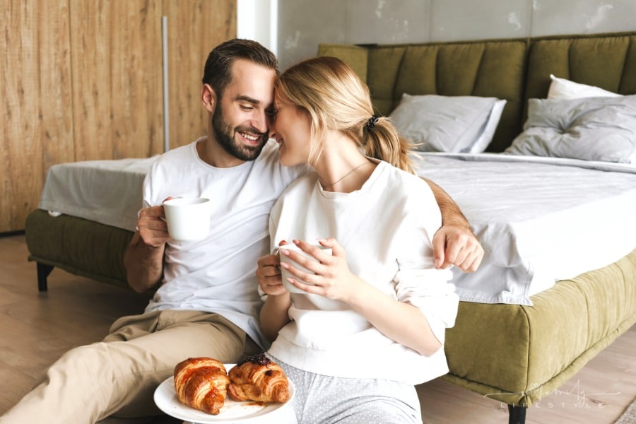 couple drinking coffee and eating croissants at end of bed