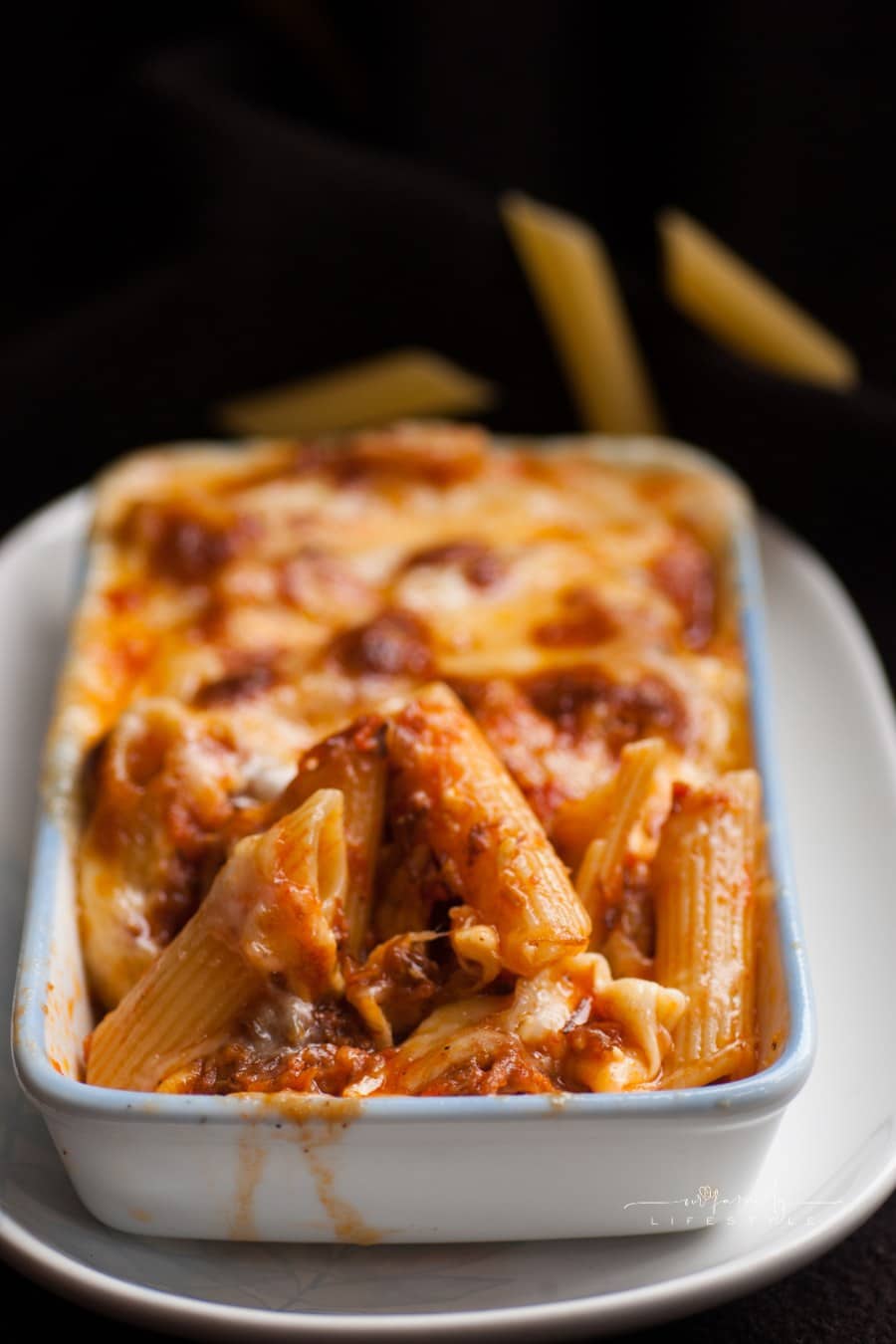 Baked penne pasta with tomato sauce and cheese in white bowl