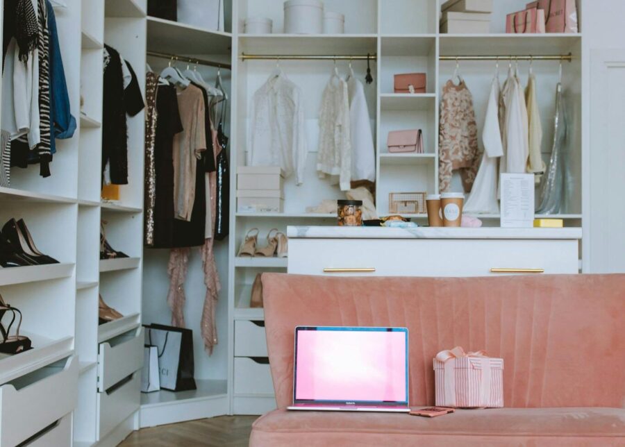 Chic dressing room with open closet, laptop on a pink couch, and stylish decor.