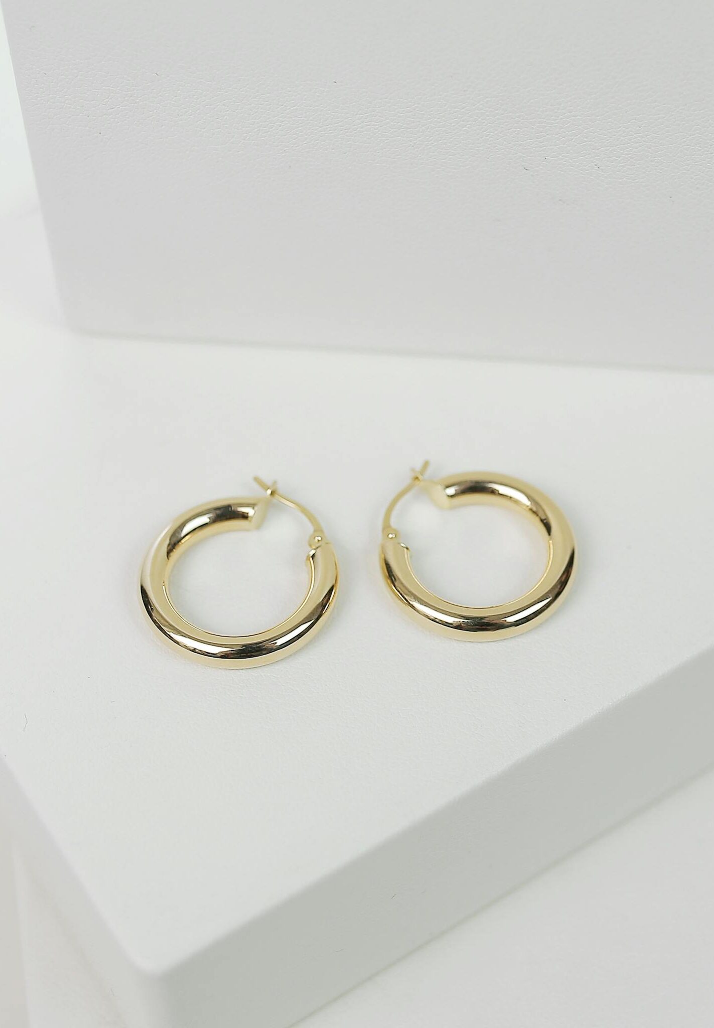 Chic gold hoop earrings displayed on a minimalist white surface, perfect for fashion collections.