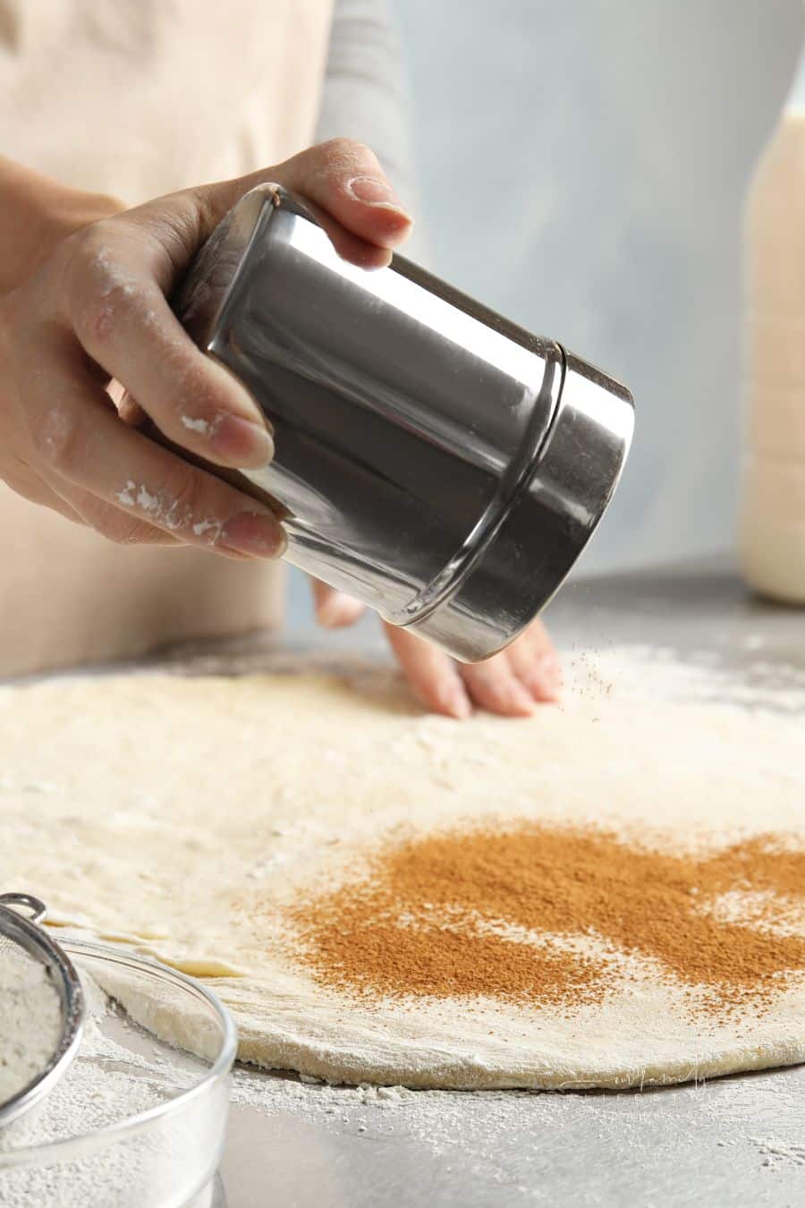 Woman Making Cinnamon Rolls at Table, sprinking cinnamon onto dough, Closeup