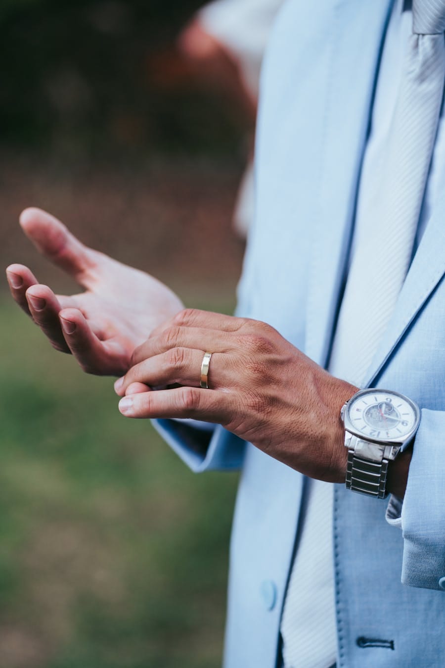 Close-up of a man's hands with wristwatch and wedding ring, wearing a suit.